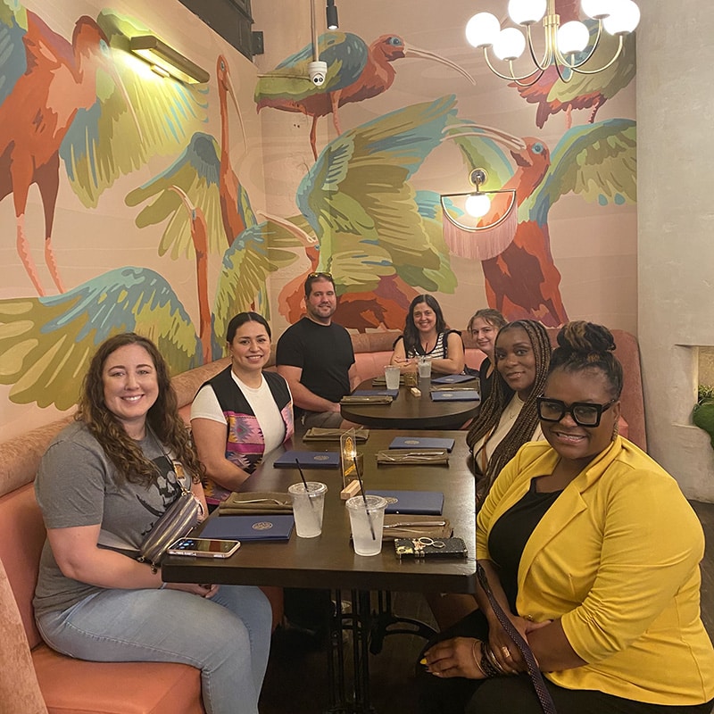 A tour group eagerly awaits a bite to eat in a restaurant with colorful wall paper depicting ostriches